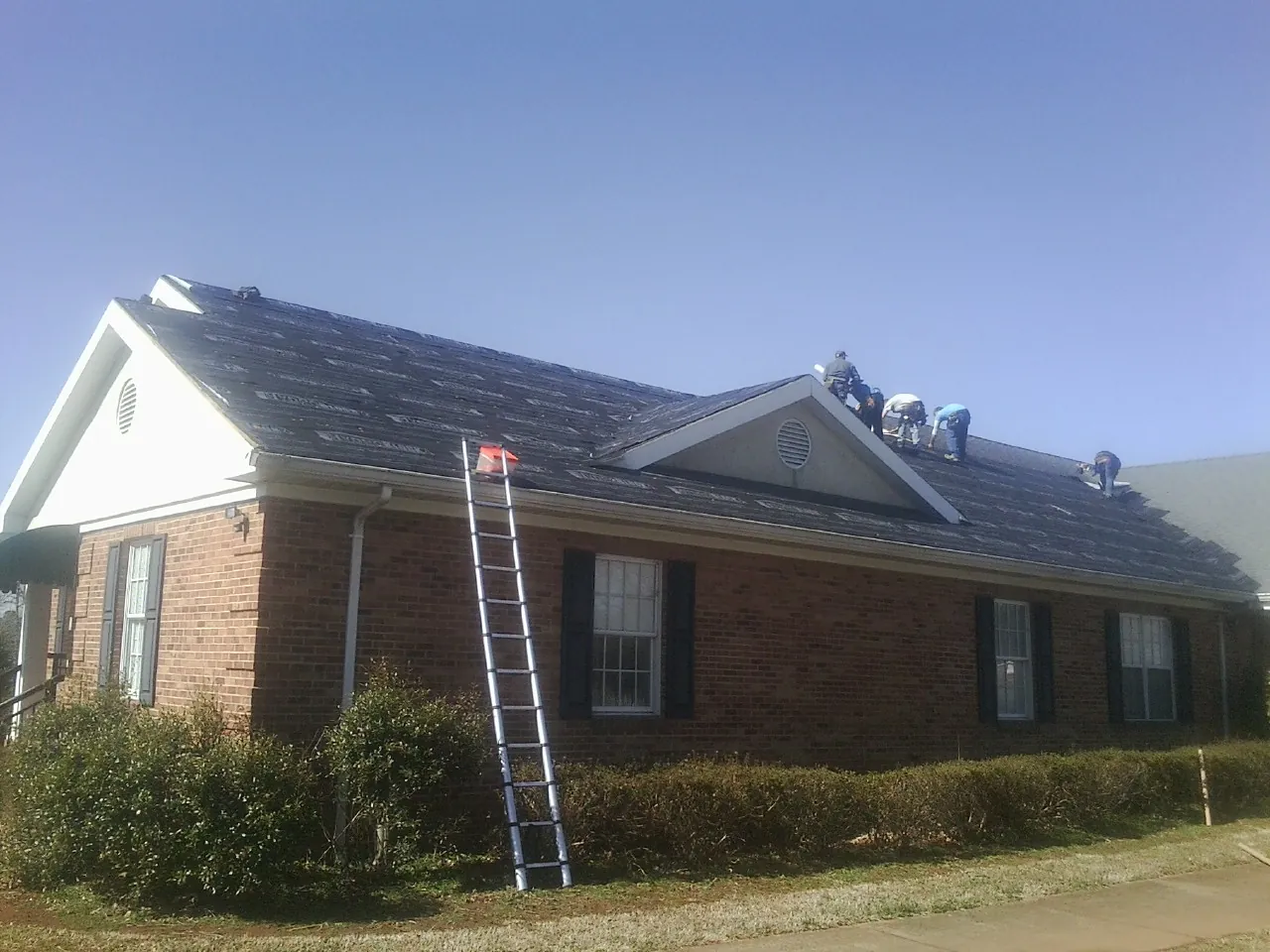 Crew tearing shingles off a brick ranch roof with a ladder set — Emergency Roof Repair work by our crew in Parker Ford