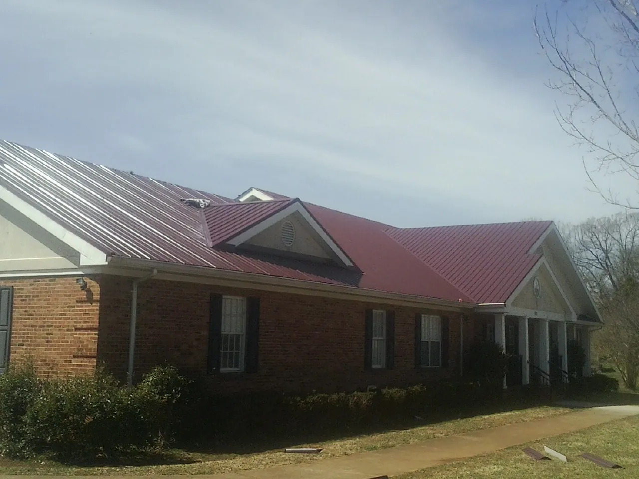 Red metal roof with gabled entries on a long brick building, from a Hail Damage Roof Repair job in Parker Ford