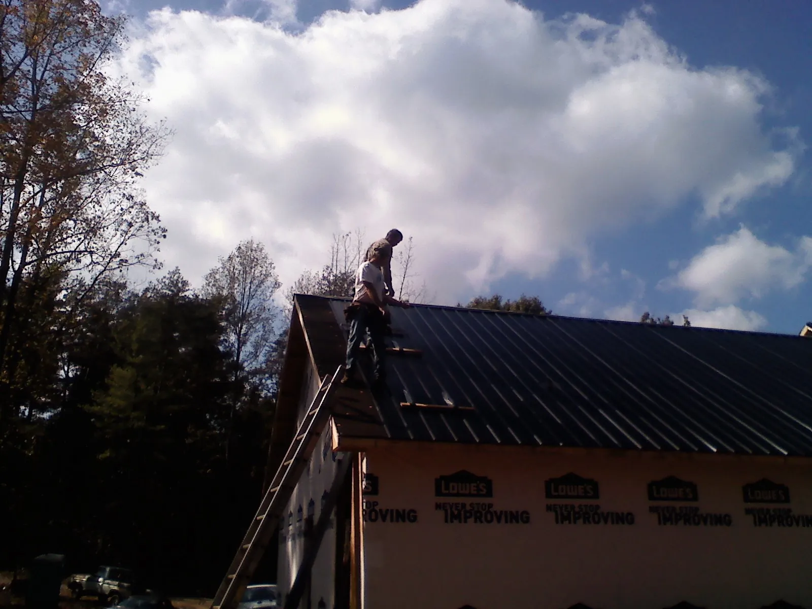 Roofer fastening dark metal panels high against a cloudy sky, from a Roof Inspection job in Parker Ford