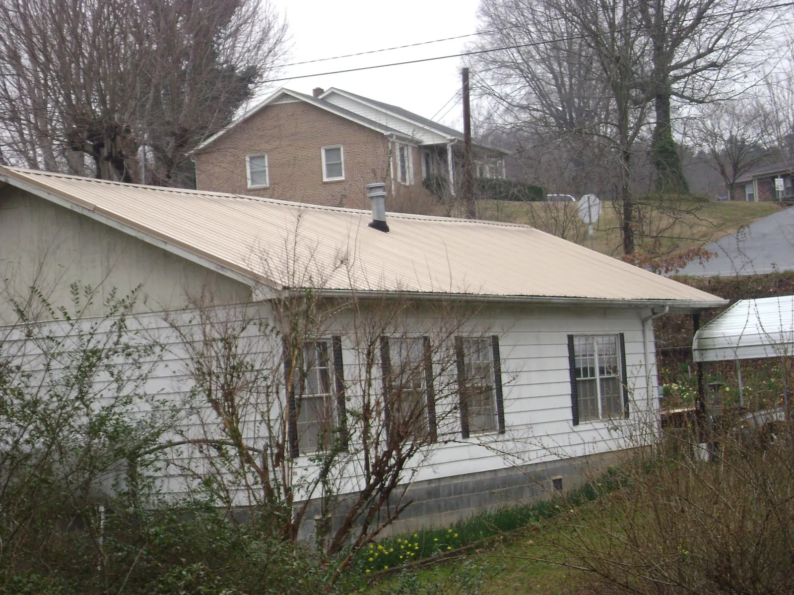 Tan metal roof on a white sided house set into a hillside — Commercial Roofing by Roofing Brothers in Parker Ford