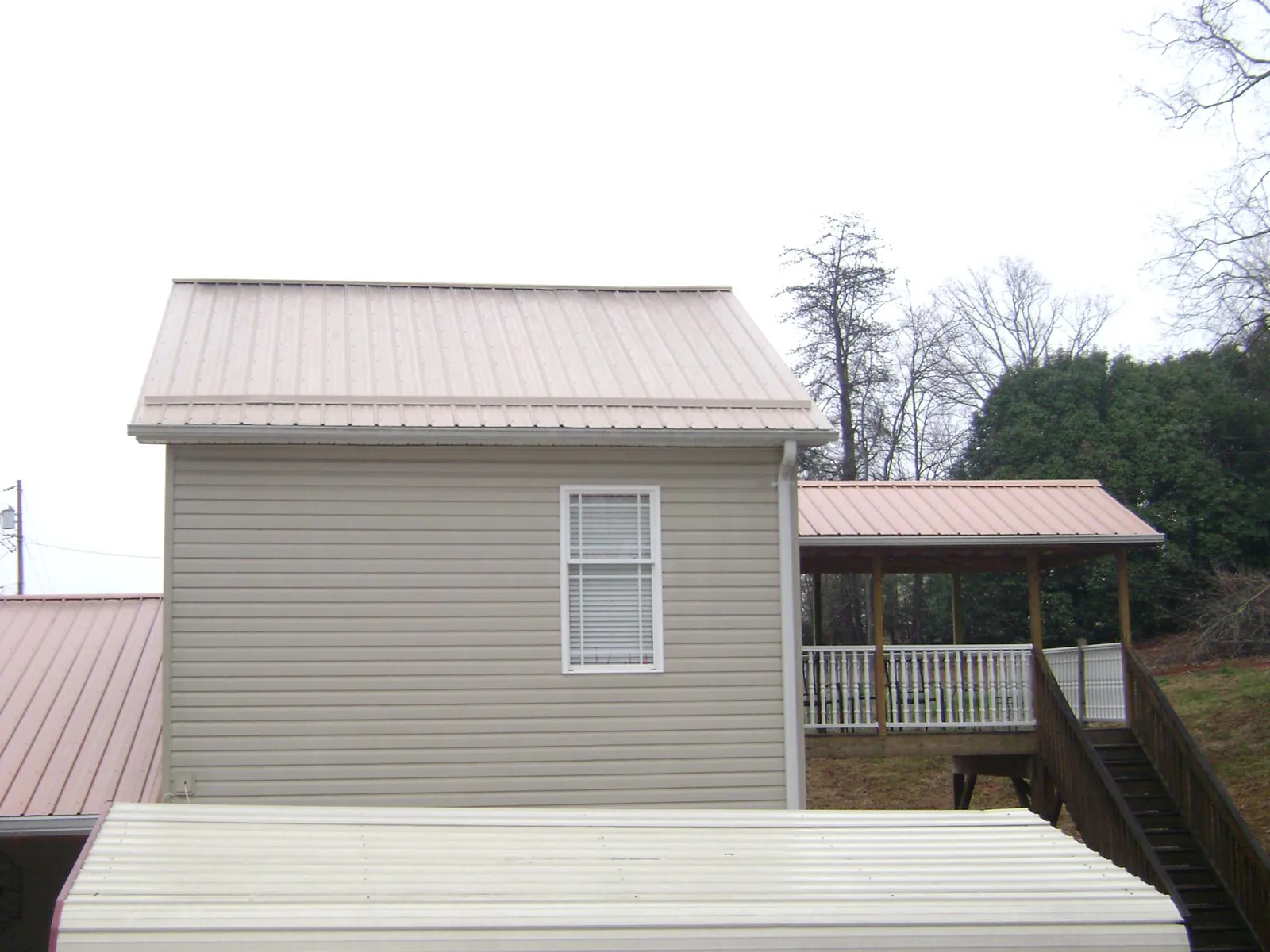 Tan metal roofs on a two story addition and attached porch, from a Roof Replacement job in Parker Ford